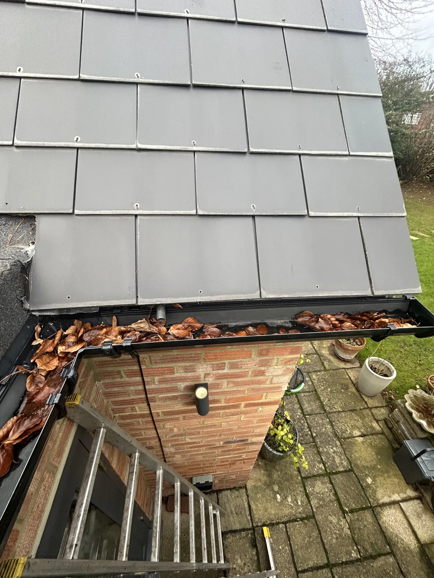 Leaf filled black gutter running along a slate clad extension roof before clearing