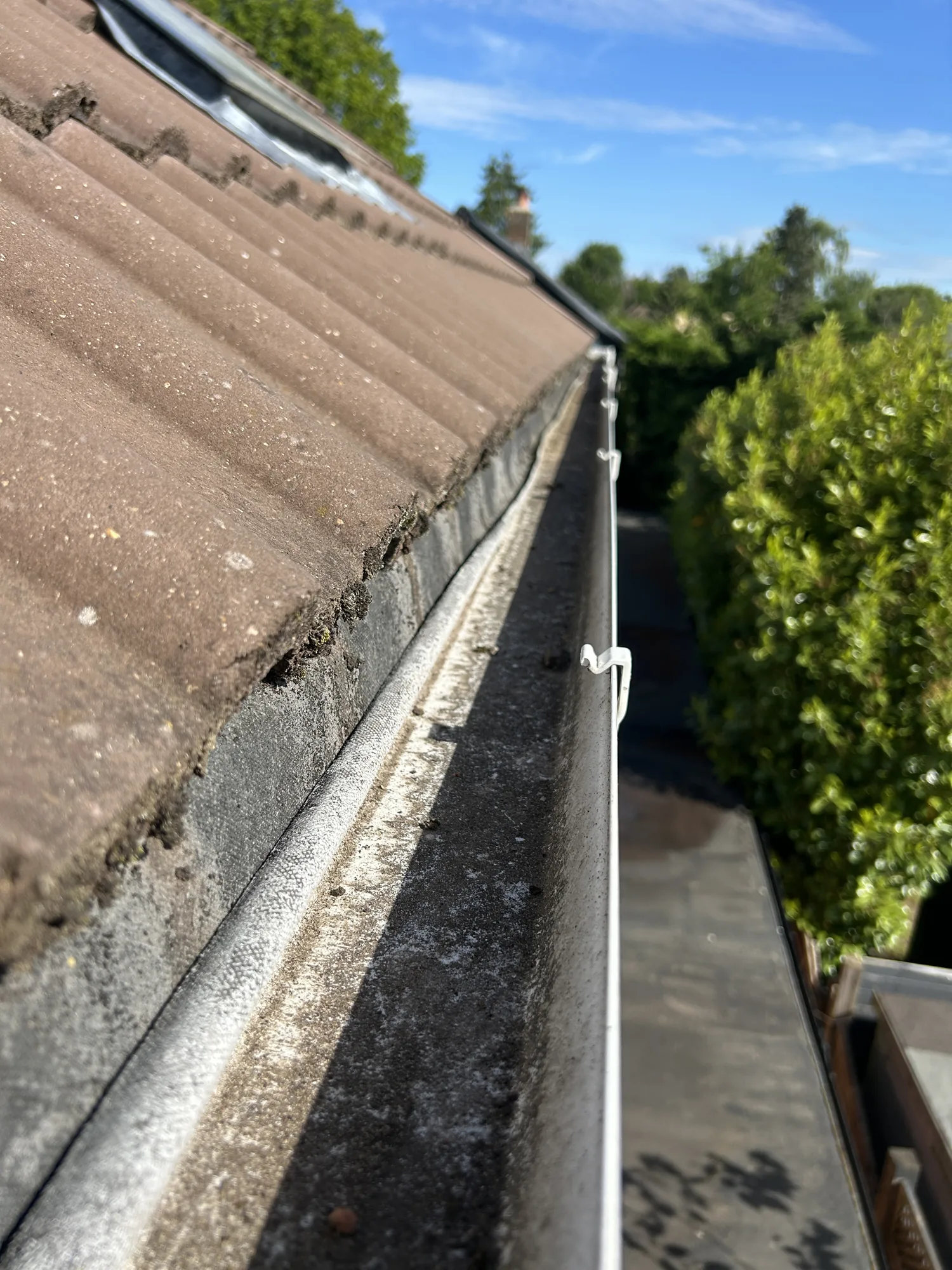 Cleared gutter run alongside a tiled roof under blue sky