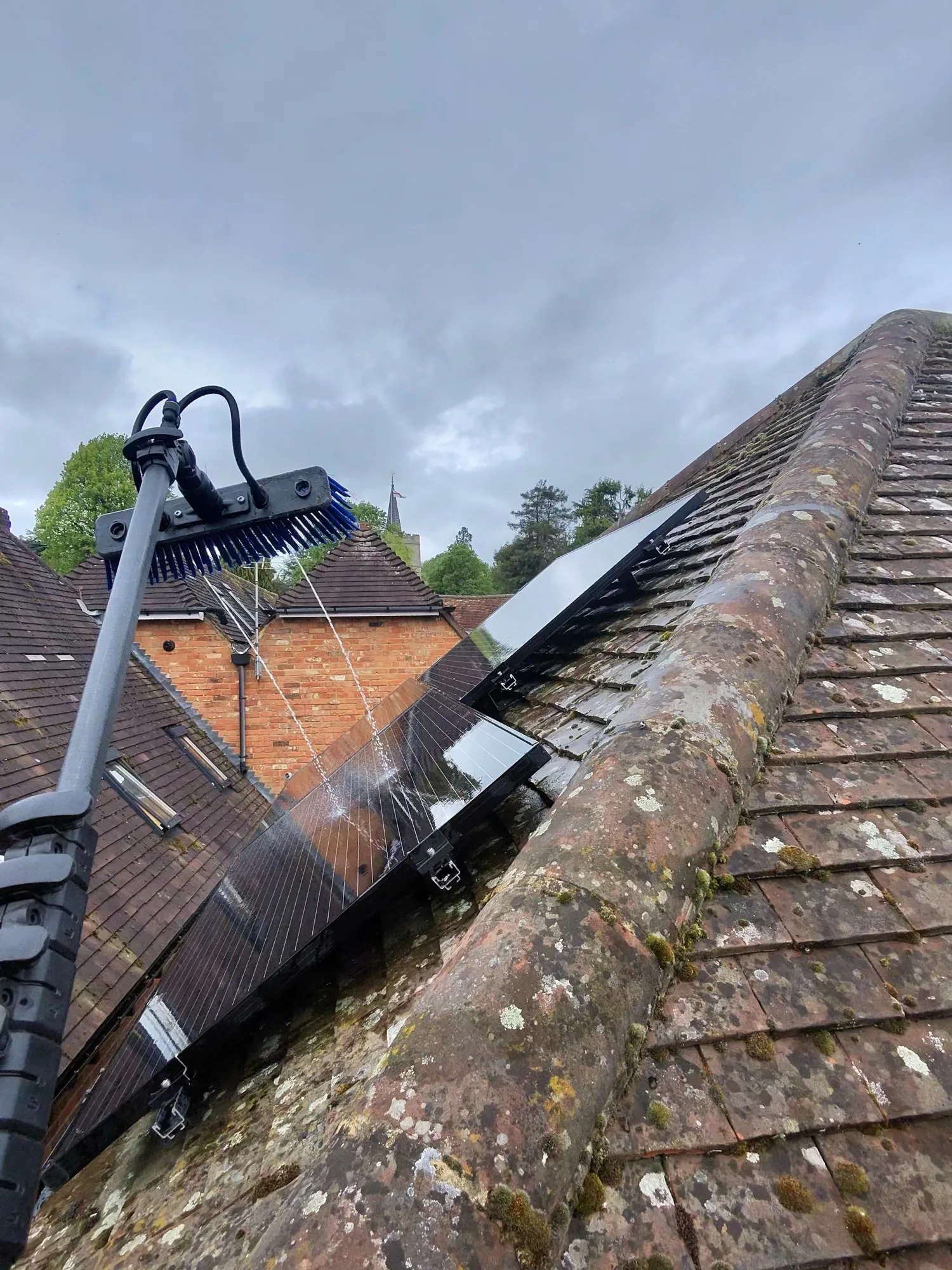 Solar panels being cleaned with a water fed pole against a village backdrop